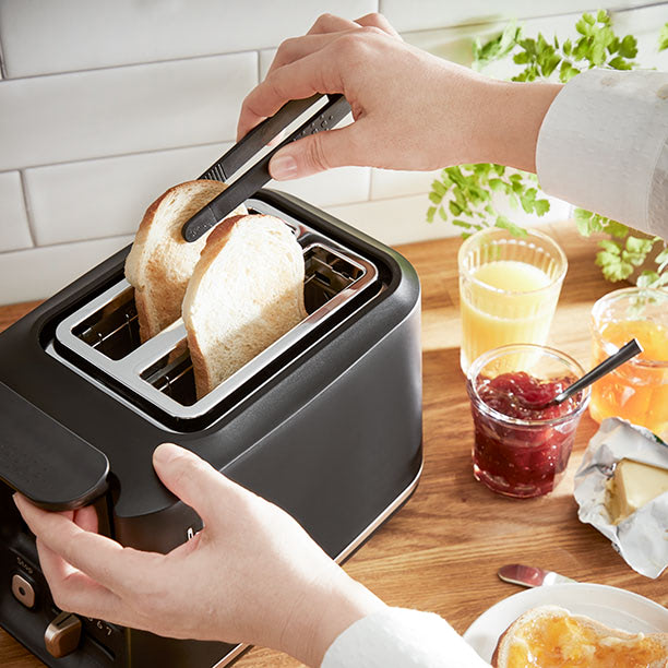 Ergonomic toaster Includeo in use: one hand picks up a toast with the included ergonomic toaster tongs